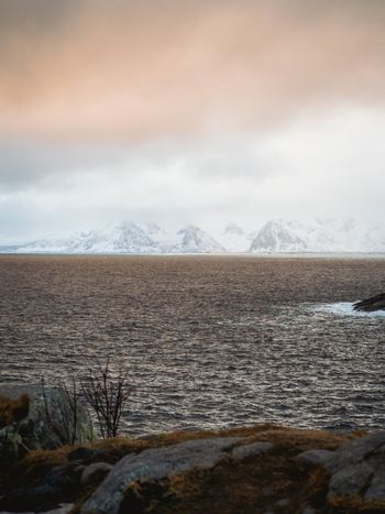 View of the tranquil sea stretching towards snow capped mountains under a muted sky a serene landscape of cold beauty Henningsv&aelig;r Nordland Norway.