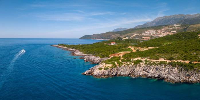 Aerial view of the rugged coastline of Aquarium Beach with turquoise waters rocky cliffs and lush green hills under a clear blue sky in Jala Vlore County Albania.