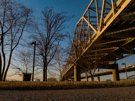 View of a massive steel truss bridge spanning the Ohio River with bare trees and a lamp post under a clear sky at sunset Louisville Kentucky United States. View of a massive steel truss bridge spanning the Ohio River with bare trees and a lamp post under a clear sky at sunset Louisville Kentucky United States.