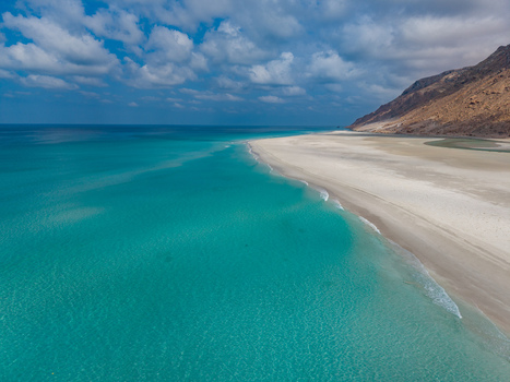 Aerial view of turquoise waters meeting pristine white sands under a sky scattered with clouds near Detwah lagoon Detwah lagoon Socotra Yemen.