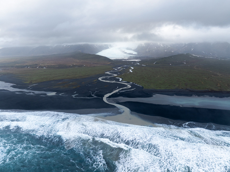 Aerial view of a glacial river flowing from the Kviarjokull glacier across dark volcanic sand plains into the Atlantic Ocean under a cloudy sky in Kviarjokull Iceland.