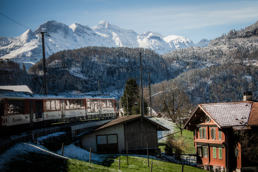 View of a train curves through a snow dusted landscape with traditional houses nestled beneath the towering snow capped Alps Train from Lucerne to Interlaken Switzerland. View of a train curves through a snow dusted landscape with traditional houses nestled beneath the towering snow capped Alps Train from Lucerne to Interlaken Switzerland.