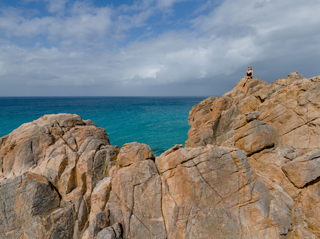 Aerial view of a woman sitting on the rocky outcrop of Castle Rock overlooking the turquoise Indian Ocean under a blue sky with scattered clouds in Dunsborough Western Australia Australia. Aerial view of a woman sitting on the rocky outcrop of Castle Rock overlooking the turquoise Indian Ocean under a blue sky with scattered clouds in Dunsborough Western Australia Australia.