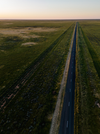Aerial view of a straight road cutting through the vast flat landscape of the outback during the golden hour in Hay New South Wales Australia.