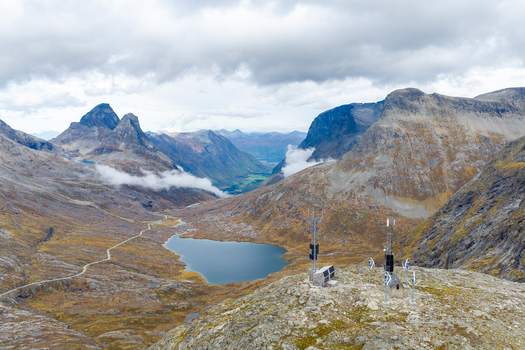 Aerial view of a rugged mountain landscape with a small lake a winding road and a communication station in the foreground in Andalsnes More og Romsdal Norway.