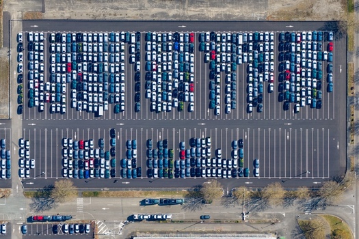 Aerial view of a vast parking lot filled with orderly rows of gleaming cars under the bright sky the geometric patterns creating a mesmerizing urban landscape Sausheim Grand Est France.