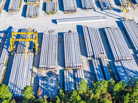 Aerial view of an industrial concrete bridge manufacturing facility with rows of steel I beams heavy machinery and storage yards in Wilmington North Carolina United States. Aerial view of an industrial concrete bridge manufacturing facility with rows of steel I beams heavy machinery and storage yards in Wilmington North Carolina United States.