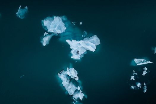 Aerial view of a person floating on an ice floe in the dark blue waters of the Vatnajokull glacial lagoon in Iceland.