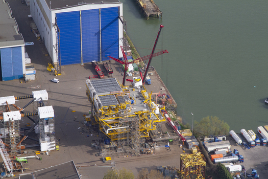 Aerial view of a large yellow offshore platform structure under construction at Rotterdam Harbour with industrial buildings and cranes in Rotterdam South Holland Netherlands. Aerial view of a large yellow offshore platform structure under construction at Rotterdam Harbour with industrial buildings and cranes in Rotterdam South Holland Netherlands.