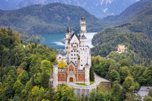 Aerial view of Neuschwanstein Castle s majestic towers reaching into the sky contrasting with the deep green forests and the serene blue of the Alpsee lake Neuschwanstein Casle Bayern Germany. Aerial view of Neuschwanstein Castle s majestic towers reaching into the sky contrasting with the deep green forests and the serene blue of the Alpsee lake Neuschwanstein Casle Bayern Germany.