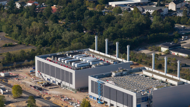 Aerial view of the Data4 Hanau data center facility featuring large cooling units on the rooftops surrounded by construction areas and lush greenery in Hanau Hessen Germany. Aerial view of the Data4 Hanau data center facility featuring large cooling units on the rooftops surrounded by construction areas and lush greenery in Hanau Hessen Germany.