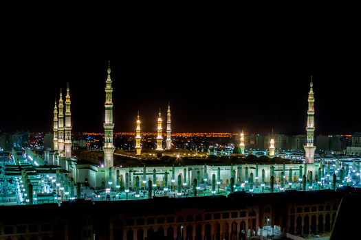 View of the illuminated Al Masjid e Nabawi at night with its towering minarets and green dome in Madinah Al Madinah Province Saudi Arabia.