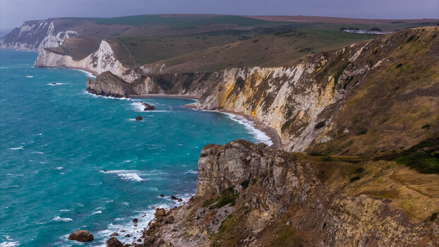 Aerial view of Lulworth Cove featuring dramatic white chalk cliffs turquoise waters and rugged coastal terrain in Wareham England United Kingdom. Aerial view of Lulworth Cove featuring dramatic white chalk cliffs turquoise waters and rugged coastal terrain in Wareham England United Kingdom.