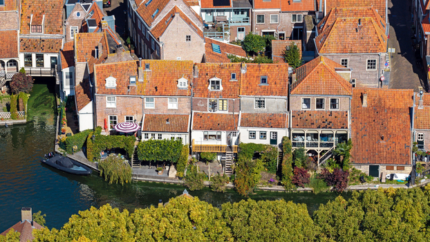 Aerial view of historic canal side houses with orange tiled roofs lush greenery and a small boat moored in the water in Enkhuizen North Holland Netherlands. Aerial view of historic canal side houses with orange tiled roofs lush greenery and a small boat moored in the water in Enkhuizen North Holland Netherlands.