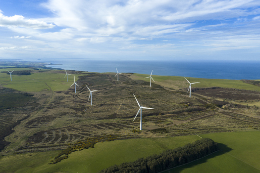 Aerial view of wind turbines on a coastal hillside overlooking the blue sea under a bright sky Scotland United Kingdom. Aerial view of wind turbines on a coastal hillside overlooking the blue sea under a bright sky Scotland United Kingdom.