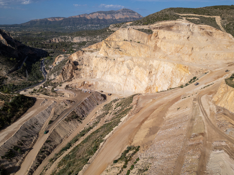 Aerial view of a large open pit quarry with terraced rock faces dirt roads and heavy machinery in Teulada Valencian Community Spain.