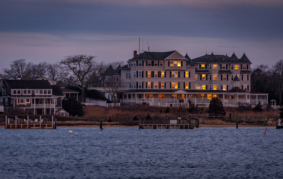 View of the historic Harbor View Hotel with glowing windows at dusk overlooking the waterfront and wooden docks in Edgartown Massachusetts United States.