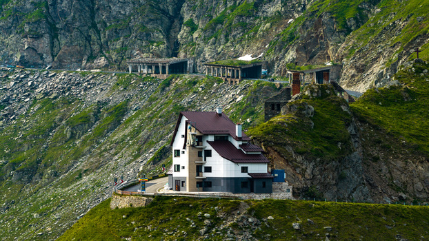 Aerial view of the Transfagarasan road featuring a modern building nestled against rocky slopes with lush green vegetation and winding road sections in Curtea de Arges Judetul Arges Romania.