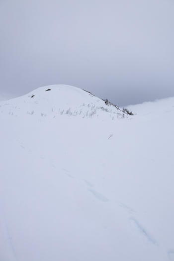 View of a snow covered mountain peak with footprints leading up the slope under an overcast winter sky in the arctic landscape Kvaloya Troms Norway.