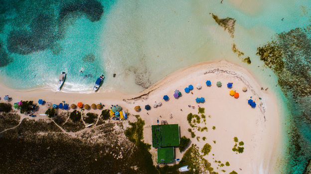 Aerial view of Los Roques archipelago with colorful beach umbrellas small boats moored on the white sand and turquoise Caribbean waters in Los Roques Dependencias Federales Venezuela. Aerial view of Los Roques archipelago with colorful beach umbrellas small boats moored on the white sand and turquoise Caribbean waters in Los Roques Dependencias Federales Venezuela.