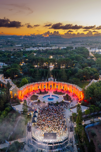Attard Malta 20 September 2026 Aerial view of Park Nazzjonali Ta Qali during an evening concert with a large crowd gathered in front of an illuminated stage and fountain under a sunset sky. Attard Malta 20 September 2026 Aerial view of Park Nazzjonali Ta Qali during an evening concert with a large crowd gathered in front of an illuminated stage and fountain under a sunset sky.