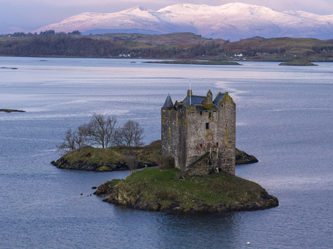 Aerial view of Castle Stalker on a small island in the calm waters of Loch Laich with snow capped mountains in the background Appin Scotland United Kingdom. Aerial view of Castle Stalker on a small island in the calm waters of Loch Laich with snow capped mountains in the background Appin Scotland United Kingdom.