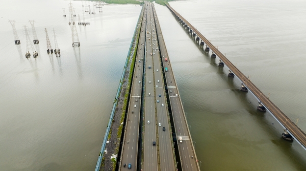 Aerial view of Vashi bridge spanning Thane Creek with traffic on the highway and adjacent railway tracks surrounded by water and transmission towers in Navi Mumbai Maharashtra India.