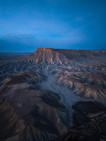 Aerial view of the rugged badlands and eroded rock formations of the desert landscape under a deep blue twilight sky in Caineville Utah United States. Aerial view of the rugged badlands and eroded rock formations of the desert landscape under a deep blue twilight sky in Caineville Utah United States.