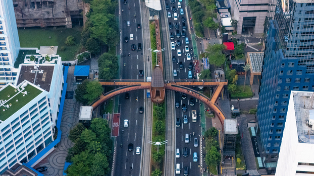 Aerial view of the Phinisi Pedestrian Bridge spanning a busy multi lane road surrounded by modern skyscrapers and urban greenery in Jakarta Indonesia. Aerial view of the Phinisi Pedestrian Bridge spanning a busy multi lane road surrounded by modern skyscrapers and urban greenery in Jakarta Indonesia.