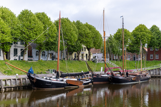 View of traditional sailing boats moored at Museumshafen Carolinensiel with lush green trees and historic buildings in Wittmund Lower Saxony Germany. View of traditional sailing boats moored at Museumshafen Carolinensiel with lush green trees and historic buildings in Wittmund Lower Saxony Germany.