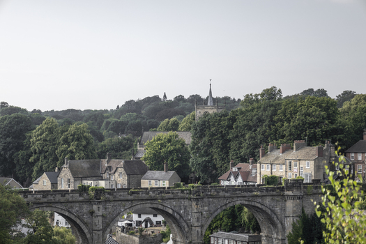 View of the historic Knaresborough Viaduct with stone buildings lush green trees and a church spire in the background in Knaresborough England United Kingdom.