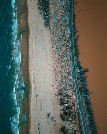 Aerial view of the narrow Langue de Barbarie peninsula with dense housing and colorful fishing boats along the riverbank in Saint Louis Saint Louis Region Senegal.