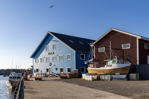 View of colorful wooden harbor buildings and fishing boats under a clear blue sky in the fishing village of Laukvik Nordland Norway. View of colorful wooden harbor buildings and fishing boats under a clear blue sky in the fishing village of Laukvik Nordland Norway.