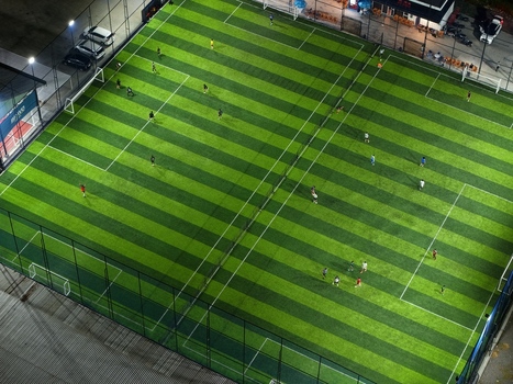 Aerial view of a night soccer match at Bravo Arena with players on the artificial turf field in Kecamatan Denpasar Selatan Bali Indonesia.