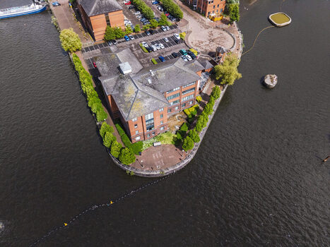 Aerial view of MediaCityUK buildings on a peninsula surrounded by the Manchester Ship Canal featuring red brick architecture and green trees in Salford England United Kingdom. Aerial view of MediaCityUK buildings on a peninsula surrounded by the Manchester Ship Canal featuring red brick architecture and green trees in Salford England United Kingdom.