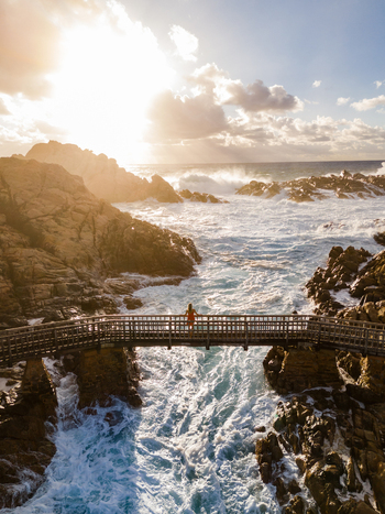 Aerial view of a person standing on the Canal Rocks Bridge over crashing waves against rugged coastal rock formations during golden hour in Yallingup Western Australia Australia. Aerial view of a person standing on the Canal Rocks Bridge over crashing waves against rugged coastal rock formations during golden hour in Yallingup Western Australia Australia.