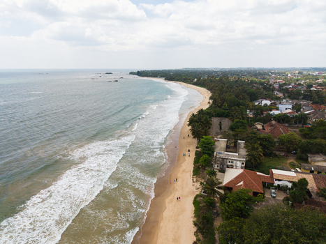 Aerial view of the sandy coastline with turquoise waves crashing on the shore palm trees and coastal buildings Matara Southern Province Sri Lanka. Aerial view of the sandy coastline with turquoise waves crashing on the shore palm trees and coastal buildings Matara Southern Province Sri Lanka.