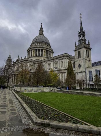 View of St. Paul s Cathedral with its iconic dome and bell tower rising above a green lawn and autumn trees under a cloudy sky in London United Kingdom.