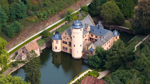 Aerial view of Schloss Mespelbrunn a historic water castle surrounded by a moat lush green forests and manicured gardens in Mespelbrunn Bayern Germany.