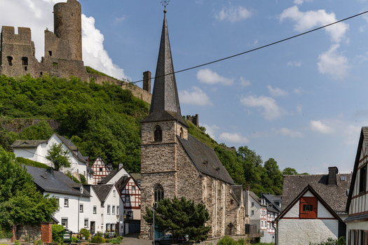 View of the Dreifaltigkeitskirche and half timbered houses with medieval castle ruins on a lush green hill in Monreal Rhineland Palatinate Germany. View of the Dreifaltigkeitskirche and half timbered houses with medieval castle ruins on a lush green hill in Monreal Rhineland Palatinate Germany.