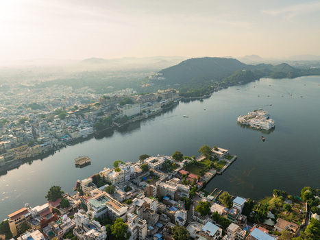 Aerial view of Lake Pichola featuring the City Palace and Lake Palace surrounded by historic architecture and lush hills in Udaipur Rajasthan India.