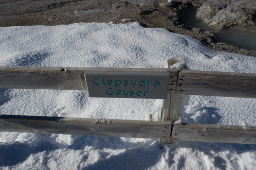 View of the Clepsydra Geyser sign mounted on a wooden fence surrounded by snow in the geothermal landscape of Yellowstone National Park Wyoming United States. View of the Clepsydra Geyser sign mounted on a wooden fence surrounded by snow in the geothermal landscape of Yellowstone National Park Wyoming United States.