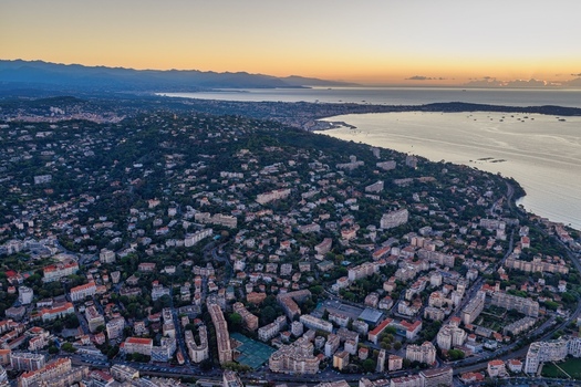 Aerial view of the coastal city of Cannes at sunset featuring dense urban architecture lush greenery and the Mediterranean Sea coastline in Cannes Provence Alpes Cote d Azur France. Aerial view of the coastal city of Cannes at sunset featuring dense urban architecture lush greenery and the Mediterranean Sea coastline in Cannes Provence Alpes Cote d Azur France.
