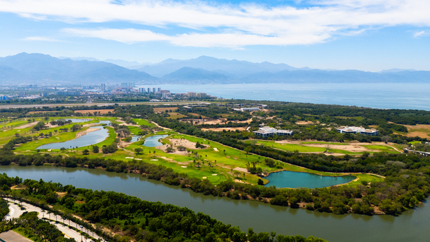 Aerial view of a lush green golf course winding along a river with the city skyline and distant mountains meeting the serene ocean Puerto Vallarta Mexico.