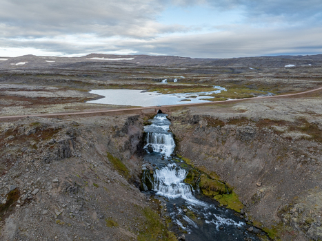 Aerial view of Dynjandi waterfall cascading down rugged cliffs into a gorge contrasting with the vast open landscape and distant mountains Westfjords Iceland. Aerial view of Dynjandi waterfall cascading down rugged cliffs into a gorge contrasting with the vast open landscape and distant mountains Westfjords Iceland.