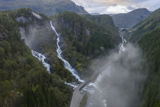 Aerial view of Latefossen waterfall cascading down rocky cliffs through lush green forests and mist near the stone bridge in Skare Vestland Norway.