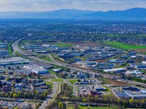 Aerial view of sprawling urban landscape highways cutting through the city mountains standing tall in the distance a symphony of progress and nature Sausheim Grand Est France.