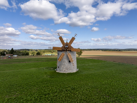 Aerial view of the historic Regi Szelmalom windmill with its wooden blades set in a vibrant green field under a blue sky with scattered clouds in Tes Hungary. Aerial view of the historic Regi Szelmalom windmill with its wooden blades set in a vibrant green field under a blue sky with scattered clouds in Tes Hungary.