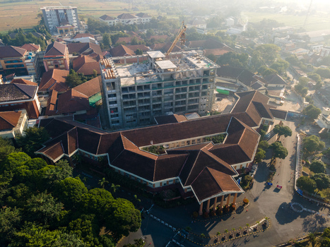 Aerial view of a building complex under construction with a concrete frame surrounded by buildings with brown tiled roofs and trees in Banyumas Regency Central Java Indonesia.