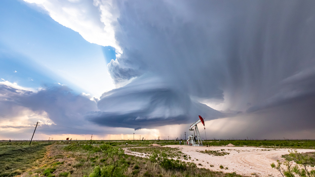 View of a dramatic supercell storm cloud hovering over an oil pumpjack in a rural field with light rays breaking through the clouds in Oklahoma City Oklahoma United States.